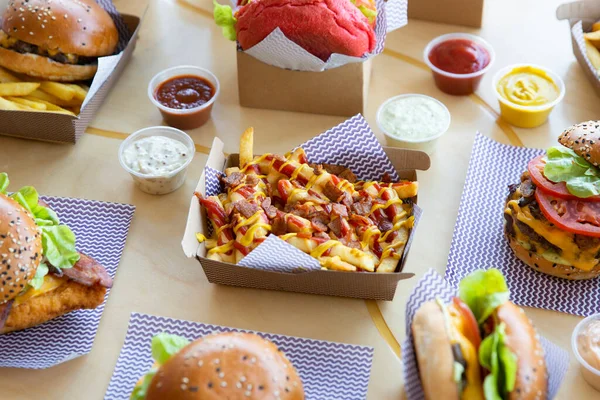 Burger restaurant layout with cheese & bacon loaded fries placed on light wooden surface.