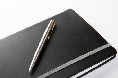 Beyaz arka planda modern siyah dergi üzerine gümüş tükenmez kalem.