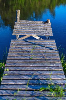 Ağaçlar yansıyan sakin ve güneşli havalarda yıpranmış iskele