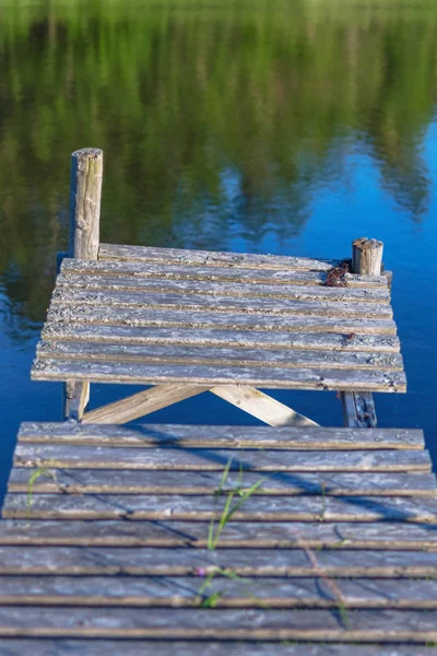 Worn jetty at calm and sunny weather with trees reflected in the — Stock Photo, Image