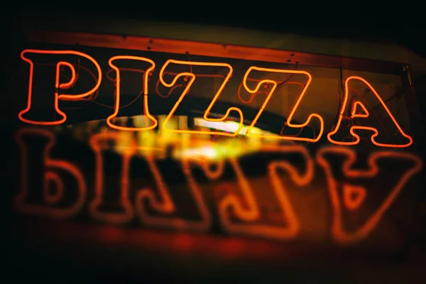 Red neon pizza sign reflected during night time