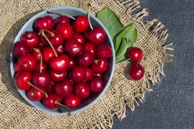 Olgun kırmızı kiraz meyve koyu arka plan ve hasır üzerinde mavi bir tabak içinde