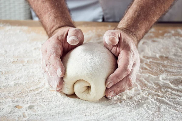 Baker hands knead dough in bright kitchen