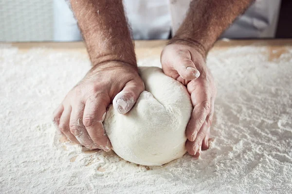 Baker hands knead dough in bright kitchen