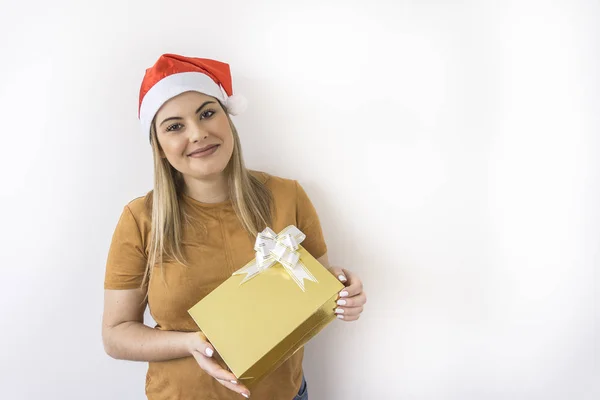 Bir altın hediye kutusu beyaz arka planda tutan giyen Noel şapka, gülümseyen genç kadın
