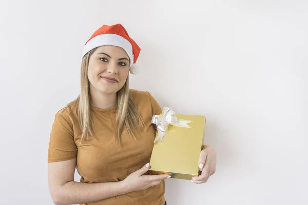 Bir altın hediye kutusu beyaz arka planda tutan giyen Noel şapka, gülümseyen genç kadın