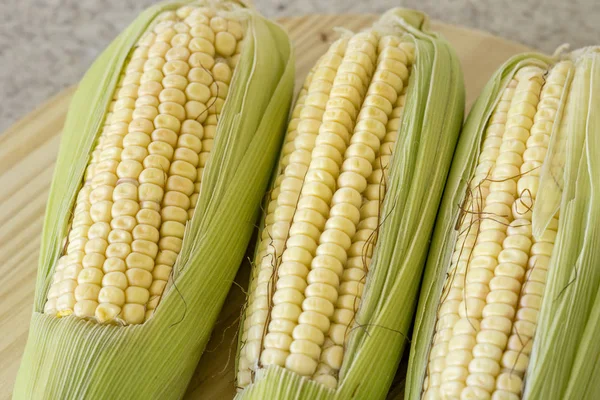 Primer plano de mazorcas de maíz crudas con paja sobre madera — Foto de Stock