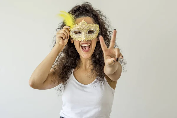 Beyaz arka planda karnaval maskesi tutan gülümseyen genç bir kadın.