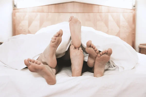 Tre par fötter liggande tillsammans under säng täcka — Stockfoto