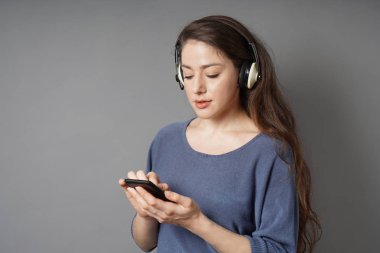 Genç kadın mobil akıllı telefon ve kablosuz bluetooth kulaklık ile müzik dinlemek