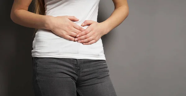 Unrecognizable young woman holding her stomach with both hands - concept for dysmenorrhea, abdominal pain, bellyache, stomachache, painful periods or menstrual cramps — Stock Photo, Image