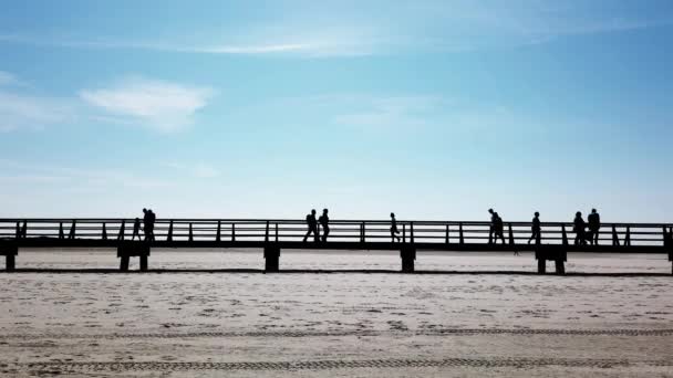 Personas en silueta caminando en la pasarela a través de la playa — Vídeos de Stock