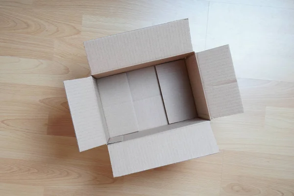 Empty cardboard box on laminate floor — Stock Photo, Image