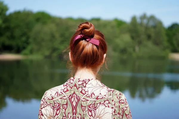 Back view of woman with red hair bun looking at lake — Stock Photo, Image