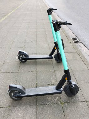 two electric kick scooters or e-scooter parked on sidewalk clipart