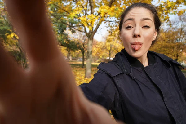 Freche junge Frau in ihren Zwanzigern streckt ihre Zunge heraus und macht ein Selfie — Stockfoto