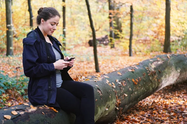 Młoda kobieta za pomocą mobilnego smartfona na zewnątrz w lesie — Zdjęcie stockowe