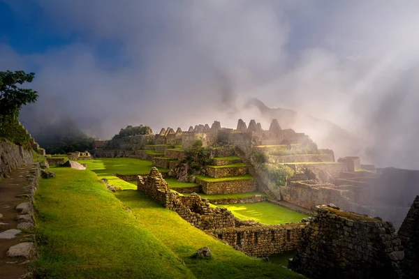 Machu Picchu şehir kalıntıları üzerinde mistik görünümü bulutların yalak geçen güneş ışınları ile sis ile kaplı. Gün doğumu sırasında İnka Kutsal şehir. 