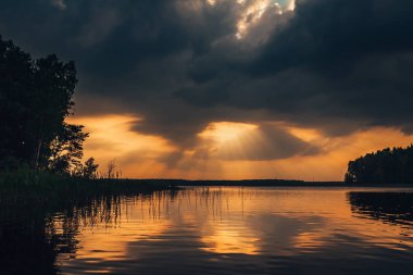 Gölde destansı gün batımı gökyüzü. Dramatik fırtınalı bulutların arasından geçen güzel güneş ışınları. İnanılmaz manzara. 
