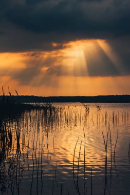 Gölde destansı gün batımı gökyüzü. Dramatik fırtınalı bulutların arasından geçen güzel güneş ışınları. İnanılmaz manzara. 