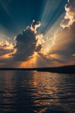 Gölde destansı gün batımı gökyüzü. Dramatik fırtınalı bulutların arasından geçen güzel güneş ışınları. İnanılmaz manzara. 