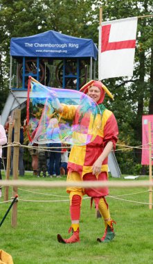 Tonbridge, İngiltere - 8 Eylül 2018: Bosco şakacı, parlak kırmızı ve sarı kılık, giyinmiş onun hareket Tonbridge bir şatoda Ortaçağ Fuarı'nda büyük bir sabun köpüğü üretir