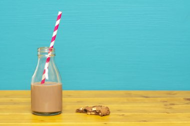 Üçte bir bardaklık süt şişesi yarısı çikolatalı milkshake, yarısı retro pipet ve yarısı yenmiş çikolatalı kurabiye ile dolu.