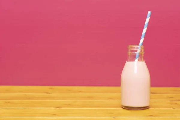 ピンクを背景にした木のテーブルの上に 3分の1ピントガラスのミルクボトルにレトロな紙の藁でイチゴのミルクシェイク — ストック写真
