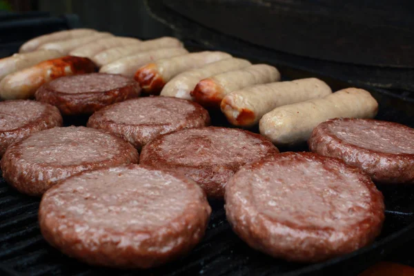 Burgers and sausages starting to cook on a grill — Stock Photo, Image
