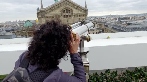 Woman looking on Paris landscape with Eiffel Tower on Lafayette Gallery terrace with coin operated binocular telescope