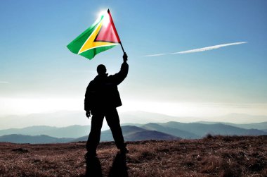 dağ tepe üstünde dalgalanan Guyana bayrak tutan adam silüeti