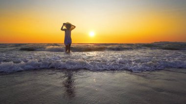 şapkalı günbatımı arka plan üzerinde beyaz elbiseli kadın