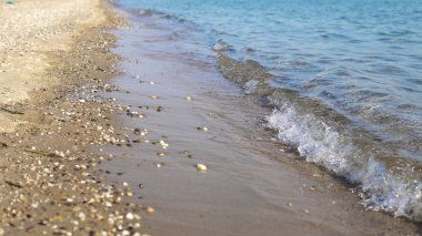 Yaz konsepti arka plan, sakin dalgalarla deniz kıyısı kumsala vuran kum ve çakıl taşları, sinematik dof