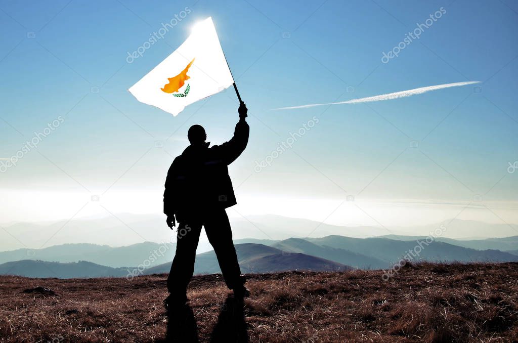 silhouette of man holding waving Cyprus flag on top of mountain peak