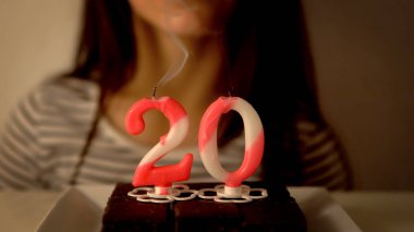 20. yaş günü mumunu bir kekin üzerine üfleyen kız.