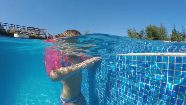 Child with arm bands relaxing in hot spring pool in geothermal spa, half underwater view