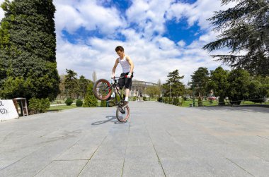 Skopje, Macedonia - circa Apr, 2013: Young BMX bicycle rider doing tricks in park outdoor  clipart