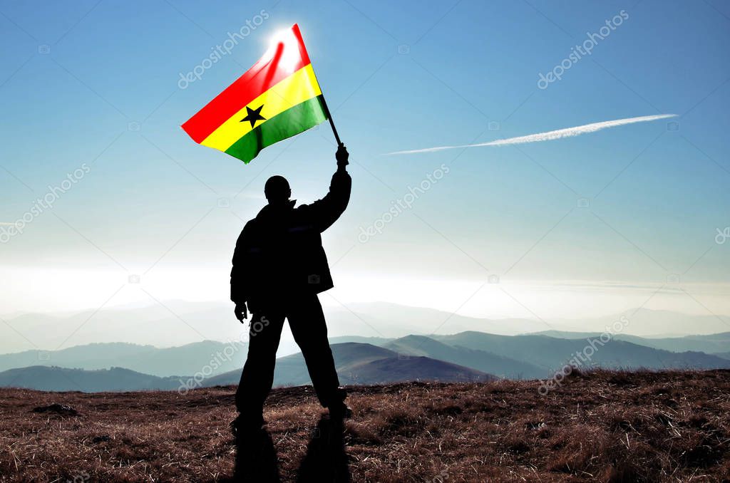 silhouette of man holding waving Ghana flag on top of mountain peak