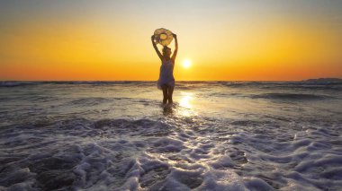 şapkalı günbatımı arka plan üzerinde beyaz elbiseli kadın