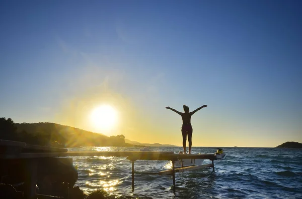 Happy woman standing arms outstretched back and enjoy life on the beach pier at Sea sunset