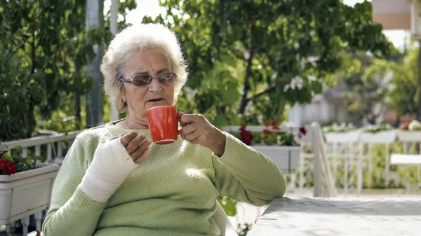 elderly old woman with injured hand sitting and drinking coffee outdoor