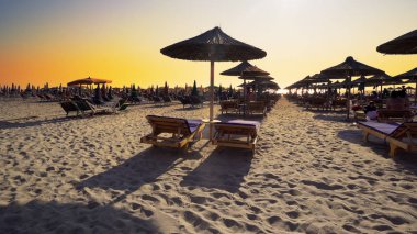 Boş plajda şezlong ve ahşap harika gün batımı tutuyor