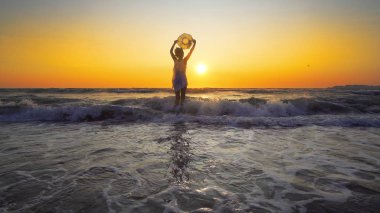 Beyaz elbiseli kadınla şapka duran dalgalar günbatımı arka plan üzerinde