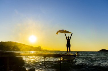 kadın sallayarak eşarp ile deniz sahilde günbatımı arka plan üzerinde dikiz 