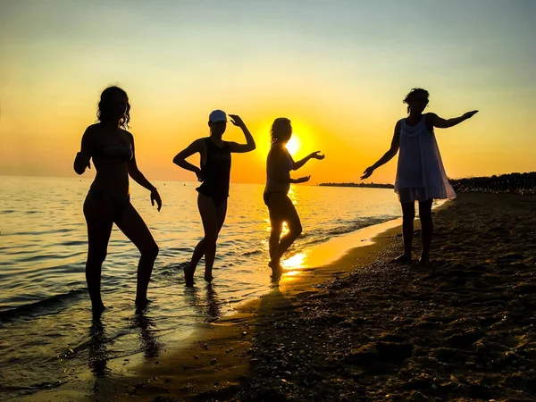 Silhouette of people dancing on beach at sunset background