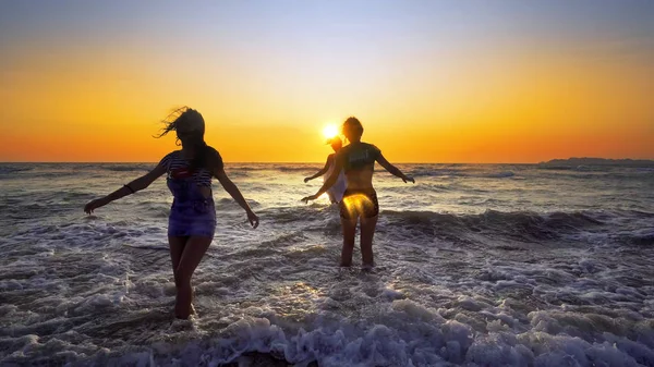 夕日を背景にビーチで海の波で楽しんで幸せな女の子のグループ — ストック写真