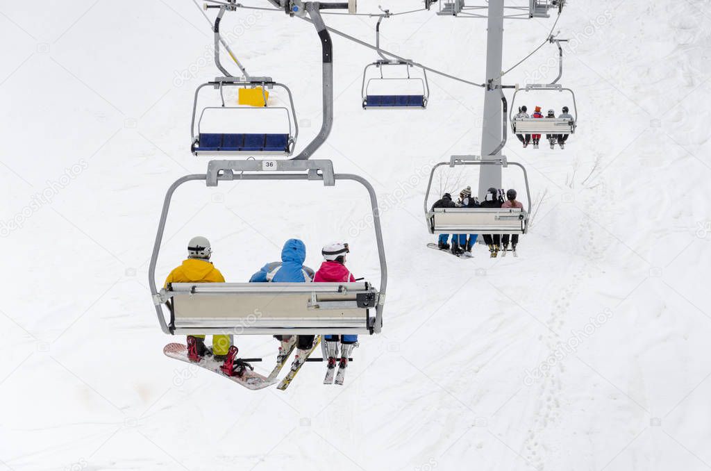 A chair lift transports skiers and snowboarders up a slope in a ski resort 