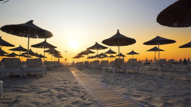 Boş plajda şezlong ve ahşap harika gün batımı tutuyor