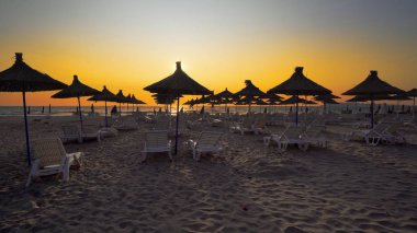 Boş plajda şezlong ve ahşap harika gün batımı tutuyor