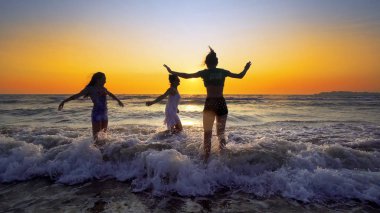 Mutlu kız eğlence günbatımı arka plan üzerinde sahilde dalgalar deniz sahip Grup